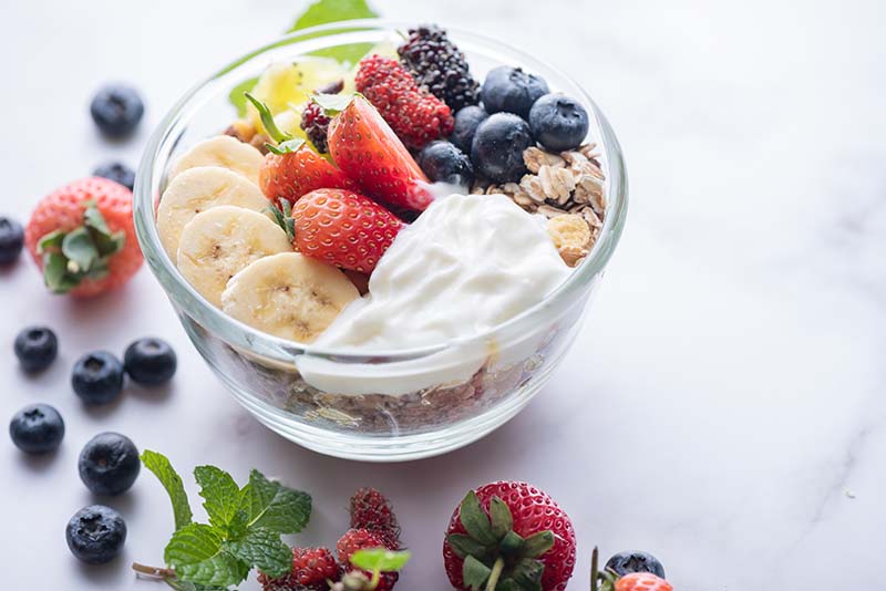 bowl-oat-granola-with-yogurt-fresh-blueberries-mulberry-strawberries-kiwi-banana-mint-nuts-board-healthy-breakfast-top-view-copy-space-flat-lay-vegetarian-food-concept