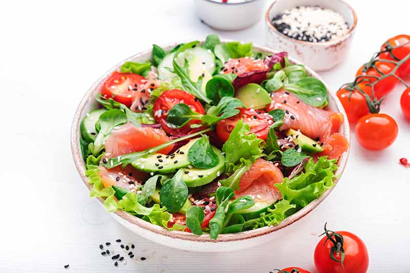 spring-salad-with-salted-salmon-avocado-tomatoes-cucumber-black-sesame-seeds-olive-oil-mixed-herbs-white-background-top-view-copy-space